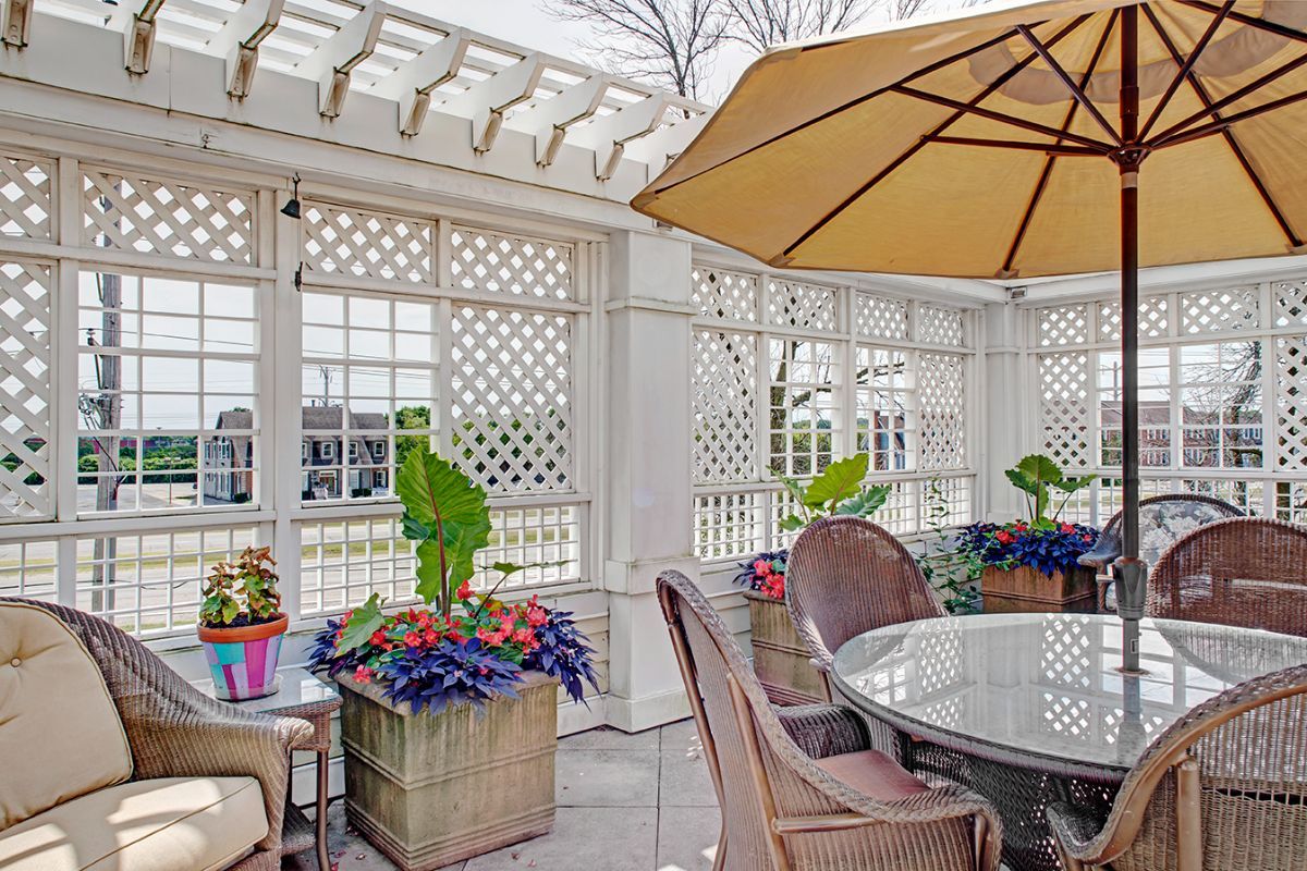 A cozy outdoor patio with a pergola, featuring a round table and chairs under an umbrella, surrounded by vibrant potted plants and flowers.