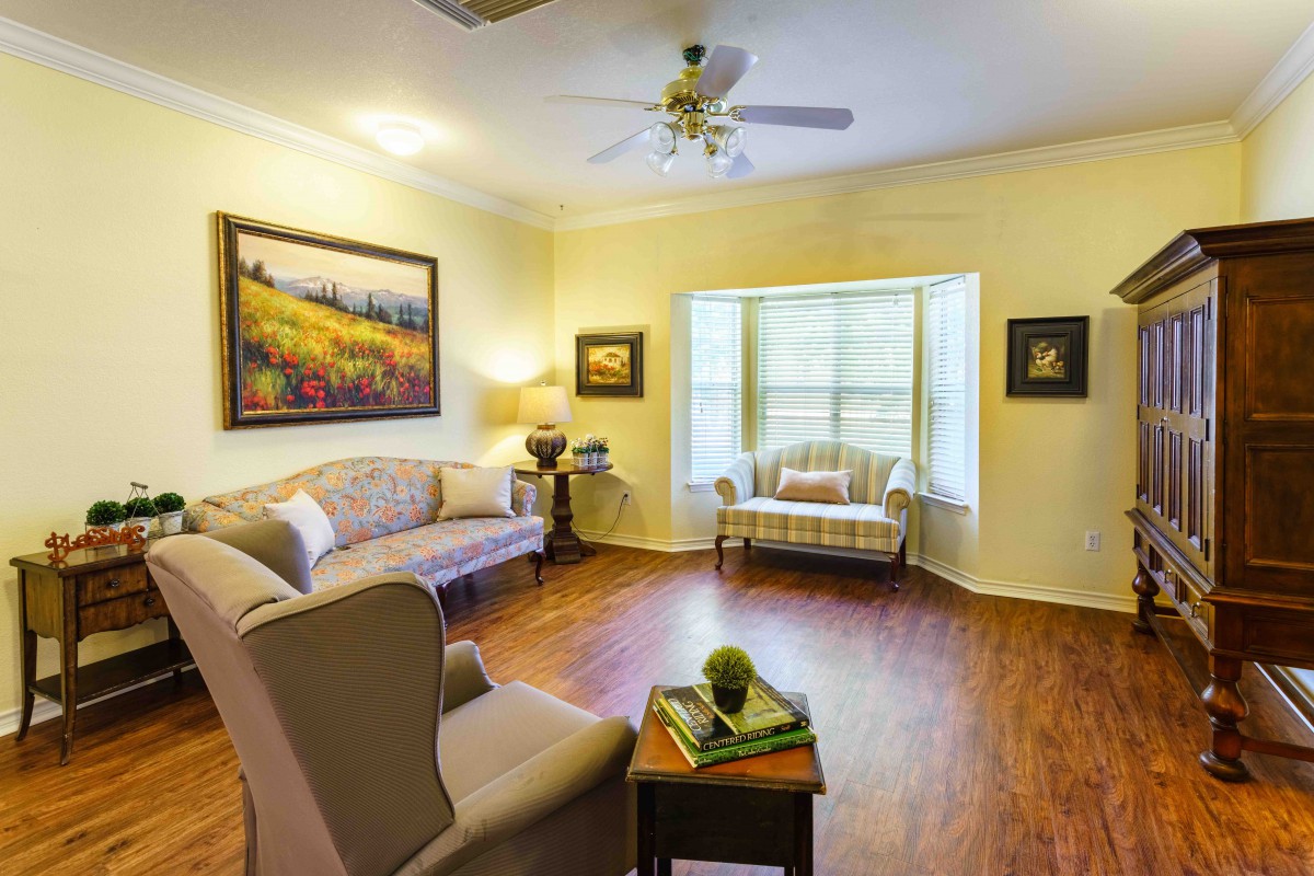 A cozy living room with elegant furniture and wooden flooring, featuring large windows and beautiful artwork.