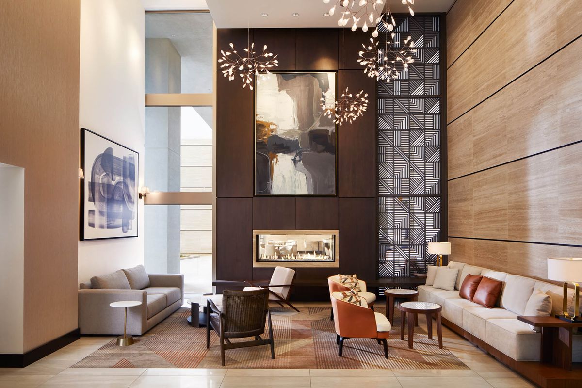 A modern and luxurious lobby featuring stylish furniture, a central fireplace, and large artwork adorning the walls.