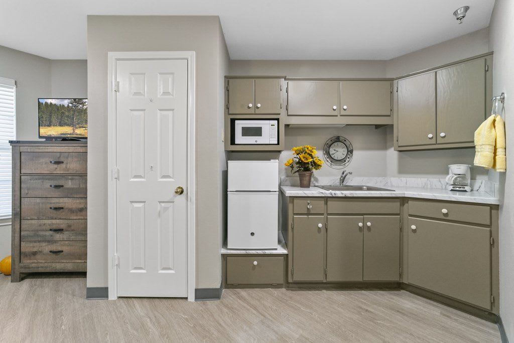 A modern kitchen with olive green cabinets, a microwave, refrigerator, and countertop space.