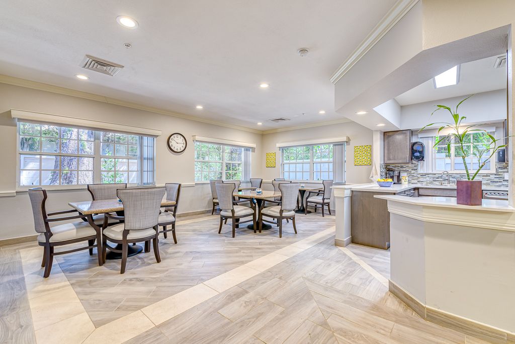 A spacious dining area with multiple tables and chairs, featuring large windows and a connected kitchen space.