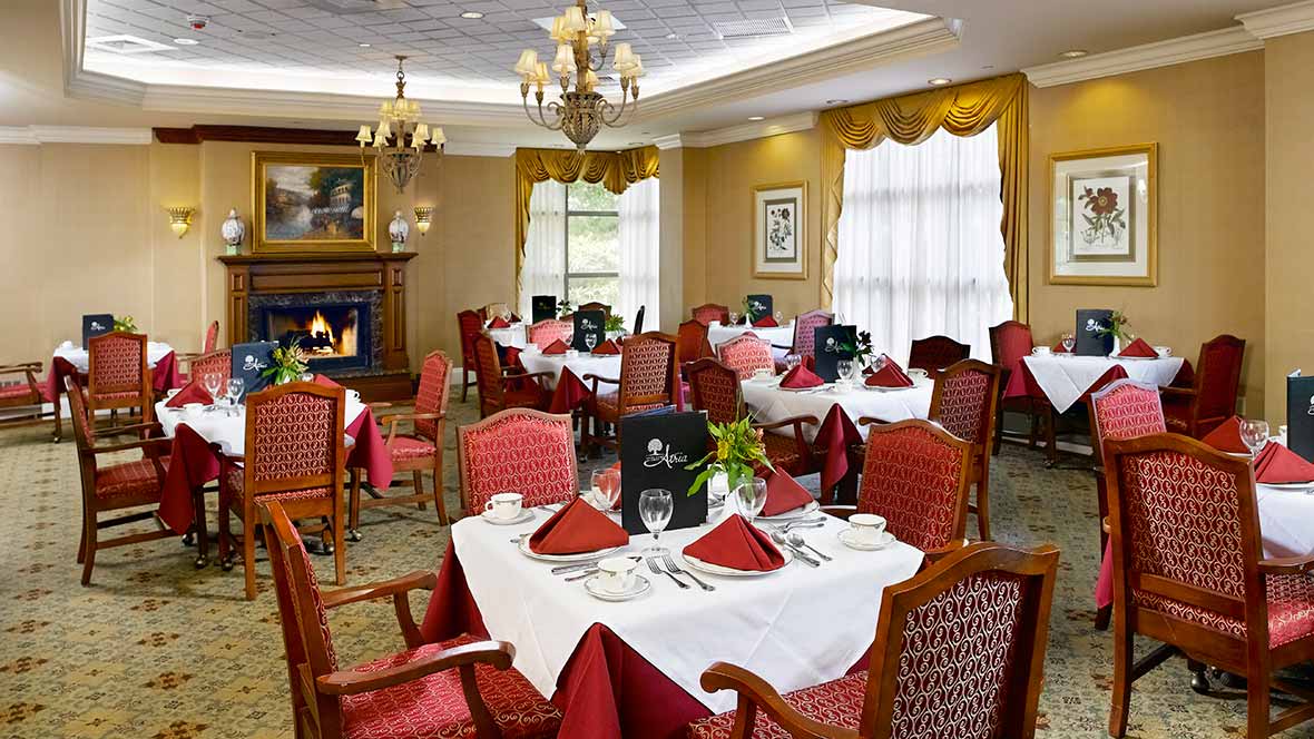An elegant restaurant dining room with neatly set tables, red and white decor, and a cozy fireplace.