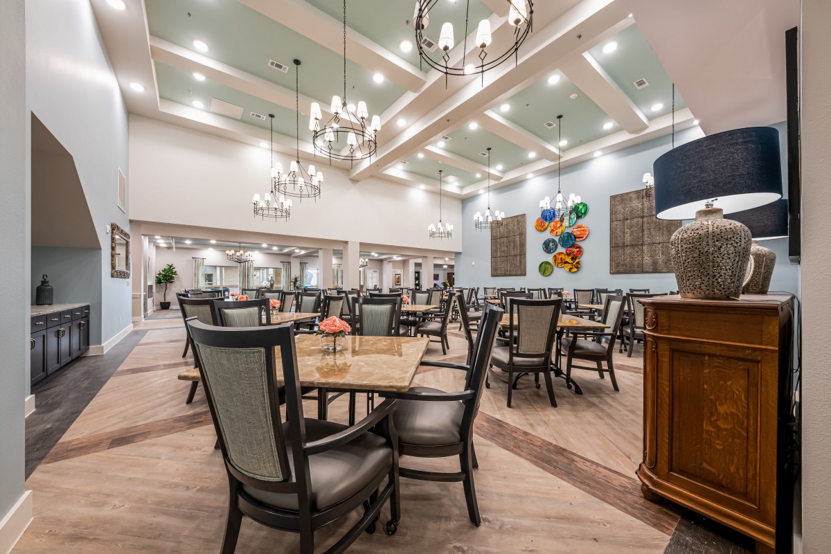A spacious and elegantly designed dining room with multiple tables and chairs, adorned with chandeliers and decorative artwork on the walls.