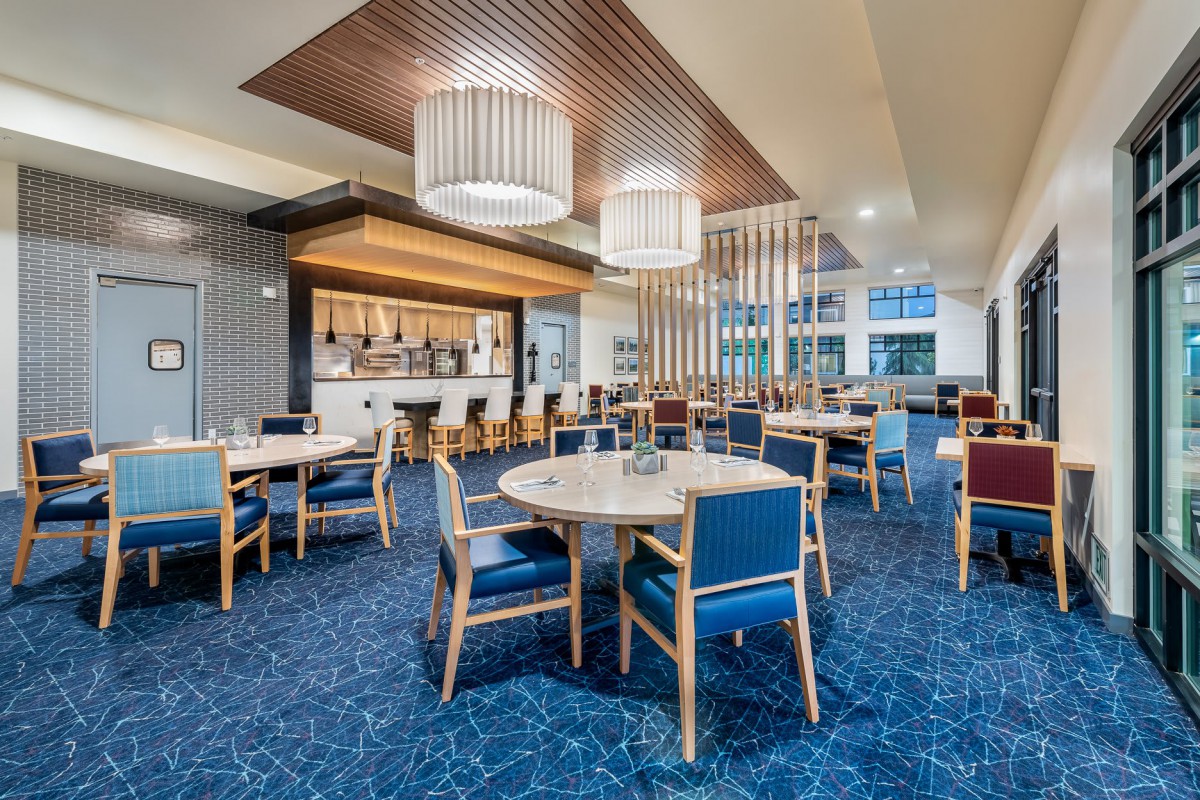 A modern restaurant interior with a dining area and bar, featuring blue carpeting and stylish lighting fixtures.