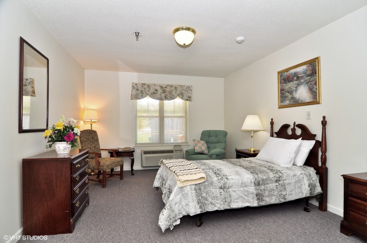 A cozy bedroom with a bed, armchair, and desk in a well-lit space.