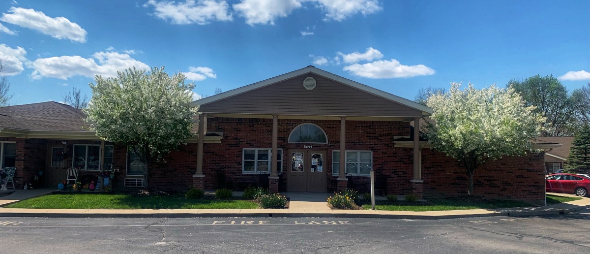 A brick building with a central entrance and a clear blue sky with clouds above.