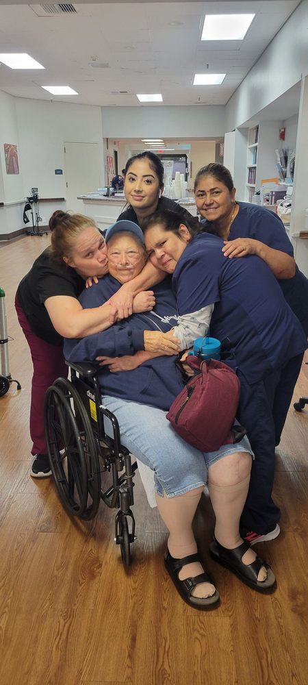 A group of people sharing a warm hug with a person in a wheelchair indoors.