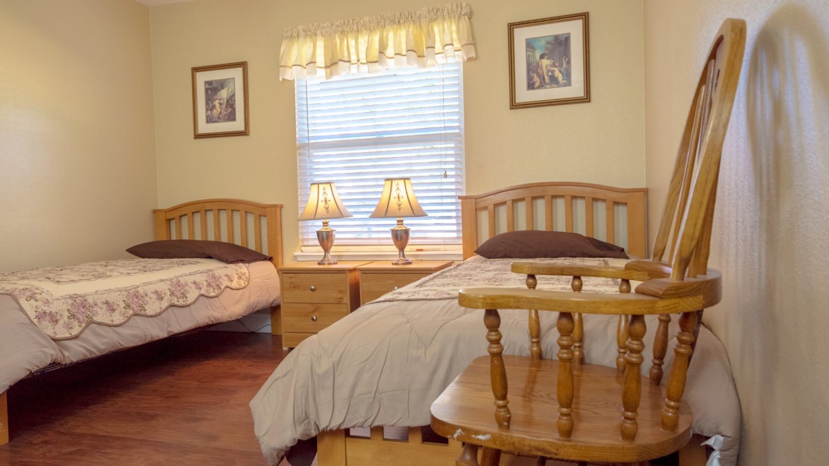 A cozy bedroom featuring two twin beds, wooden furniture, and softly glowing lamps.