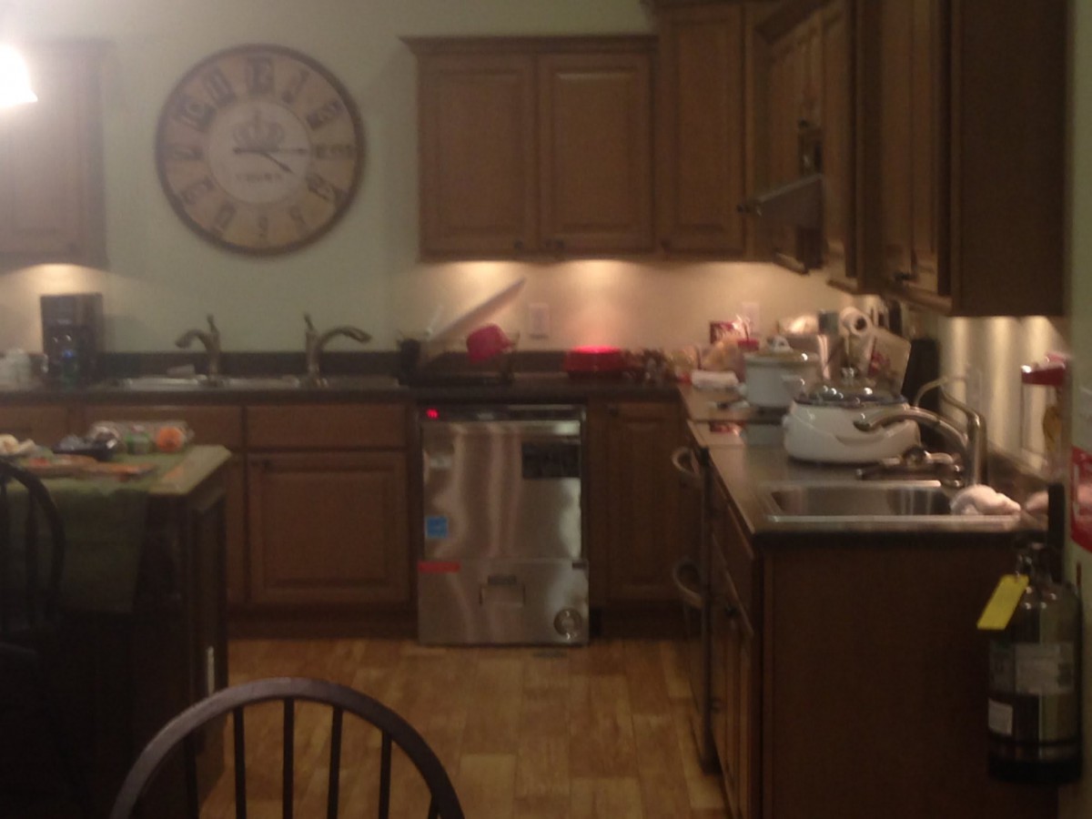 A cozy kitchen with wooden cabinets, a large clock on the wall, and various appliances on the countertop.