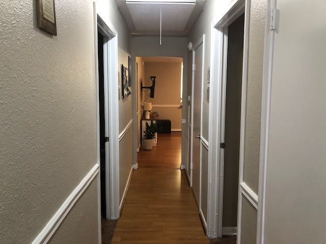 A well-lit hallway with wooden flooring and several doors on either side.