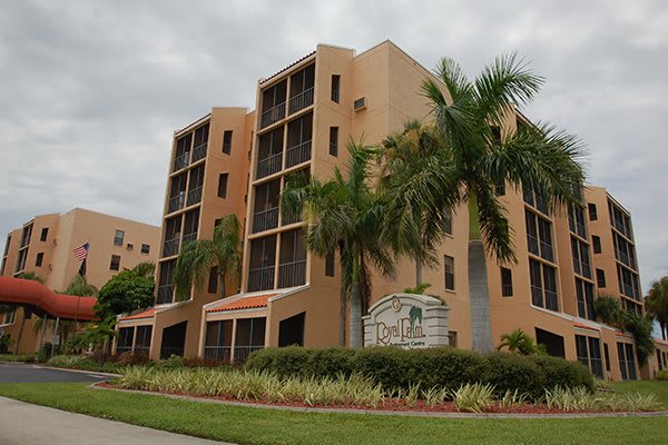 A modern apartment building with palm trees under a cloudy sky.