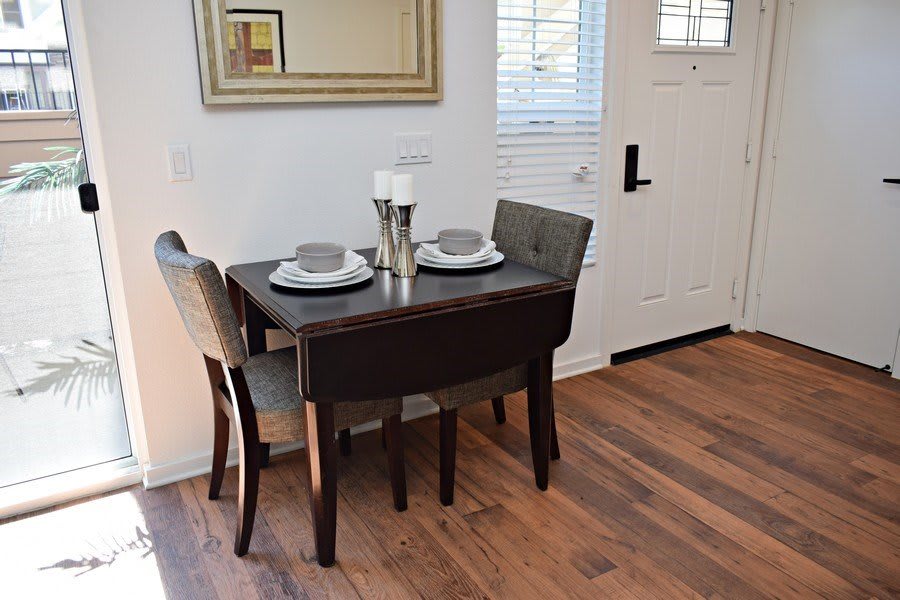 A cozy dining nook with a small table set for two, featuring elegant place settings and a wall mirror.