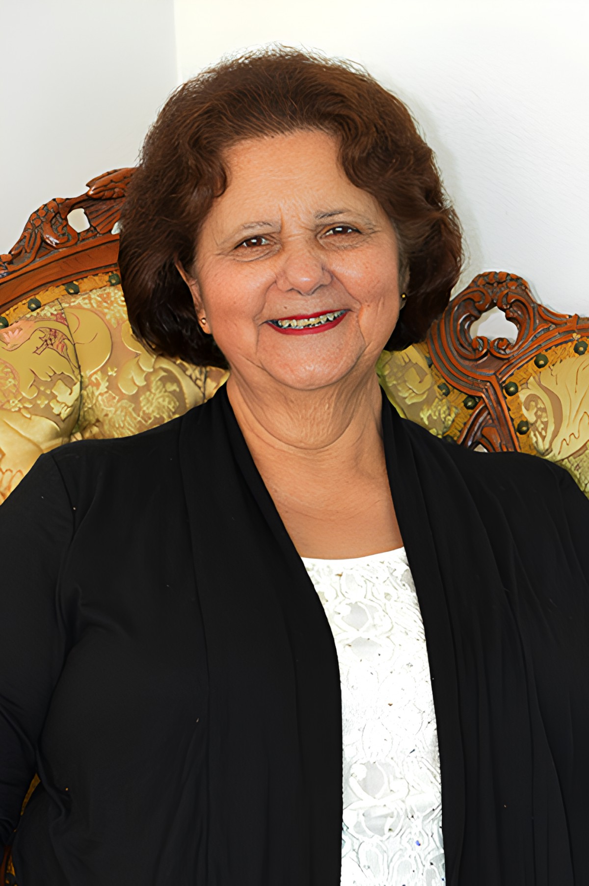 A woman sitting on an ornate chair, smiling warmly.