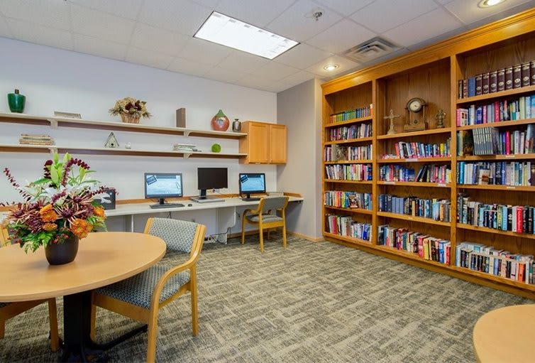 A quiet library corner with bookshelves, computers, and a table with chairs.