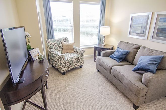 A cozy living room with a sofa, armchair, and natural lighting from large windows.