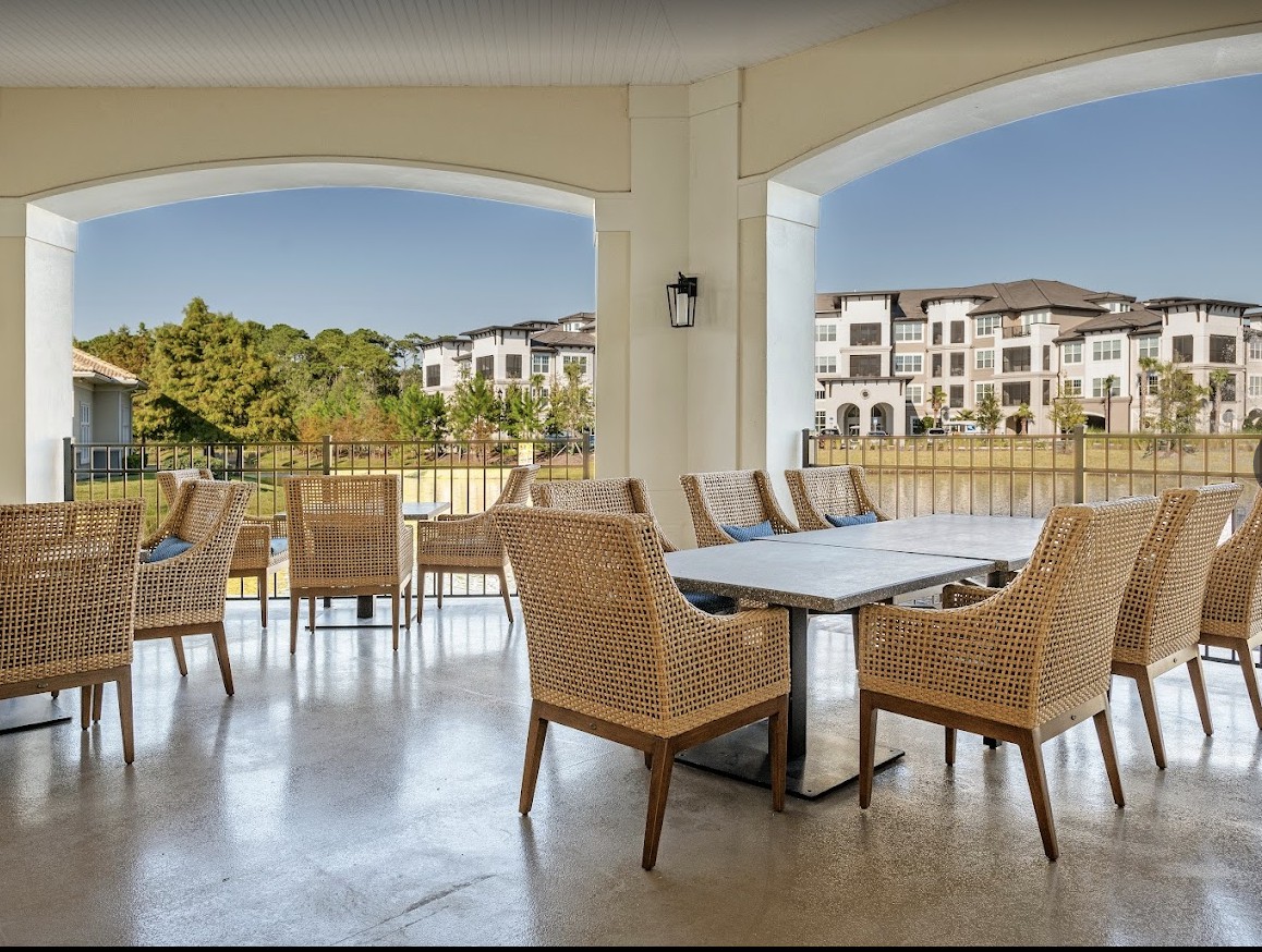 A spacious patio area overlooking an apartment complex, featuring a dining table with wicker chairs.