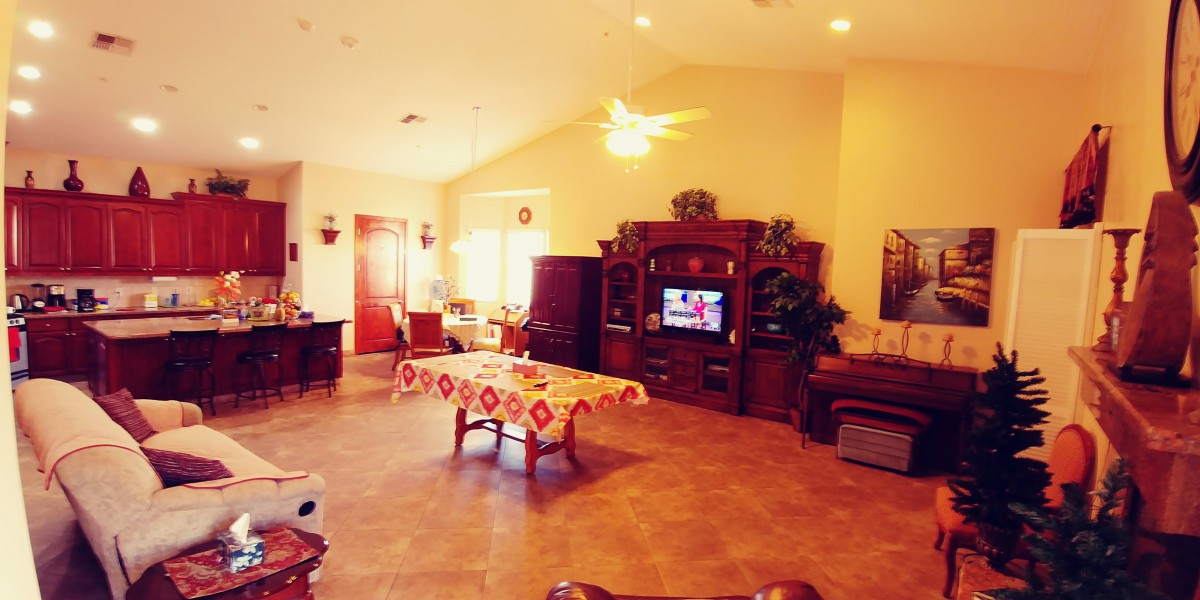 A cozy living room featuring a central table with a patterned cover, a large wooden entertainment unit with a television, and comfortable seating.