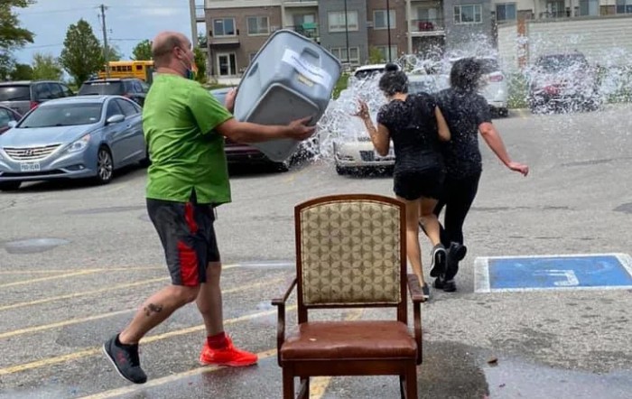 A man playfully dumps a bucket of water on two women in a parking lot.