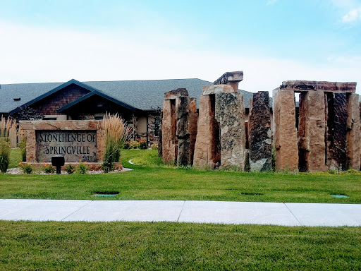 A view of a stone monument beside a modern building, set in a green landscape.
