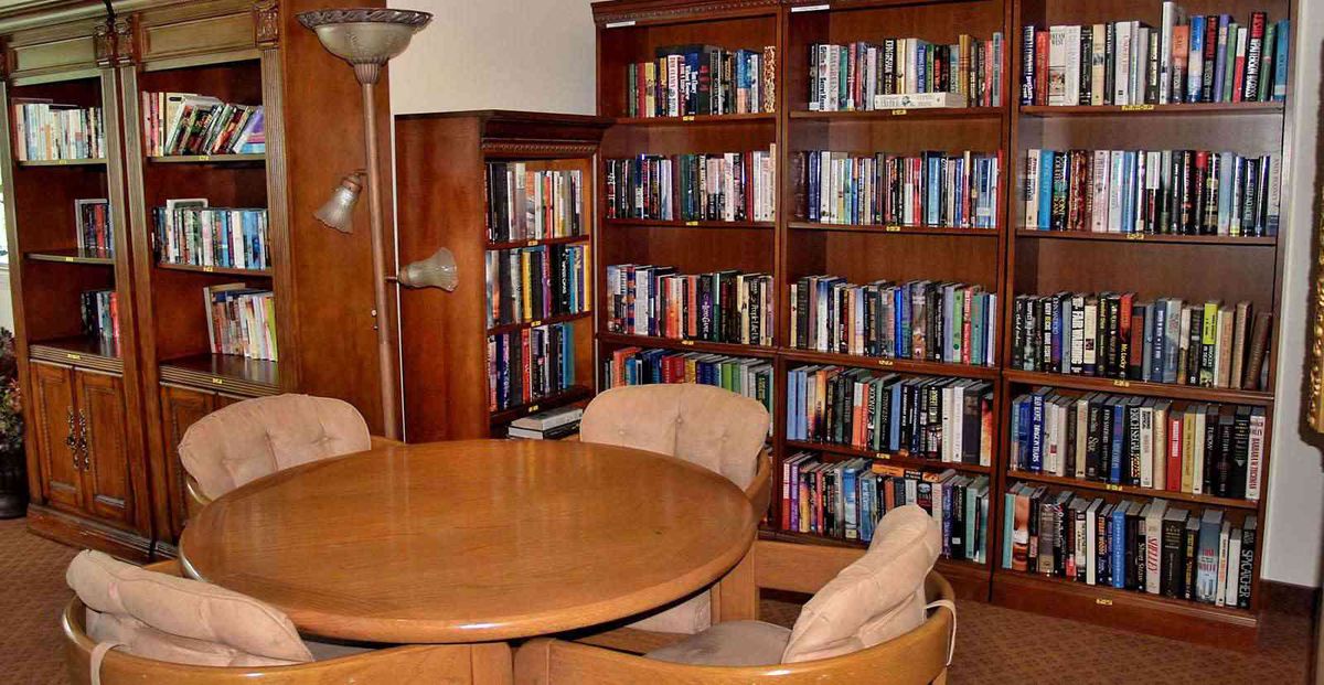 A cozy library corner featuring wooden bookshelves filled with books, a round table, and comfortable chairs.