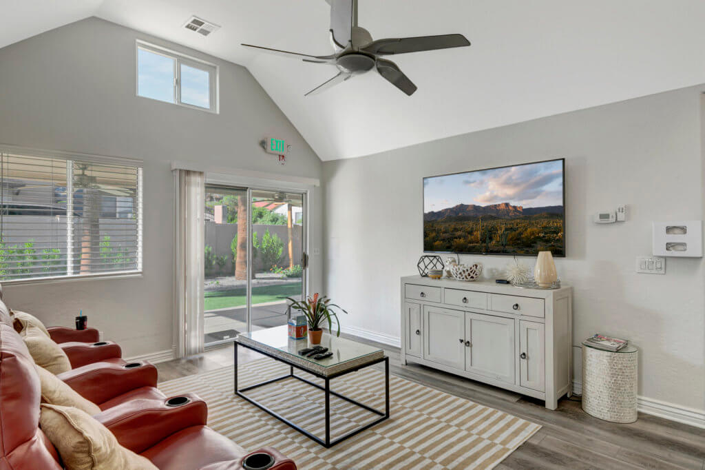 A modern living room with a ceiling fan, wall-mounted TV, and stylish decor.