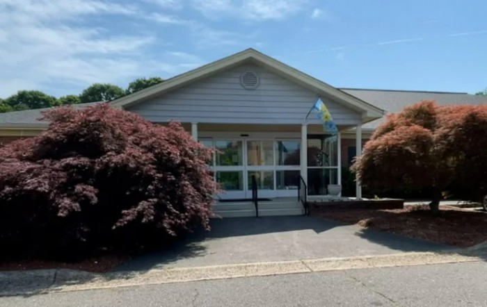 A small building with a front entrance, surrounded by trees and underneath a clear blue sky.