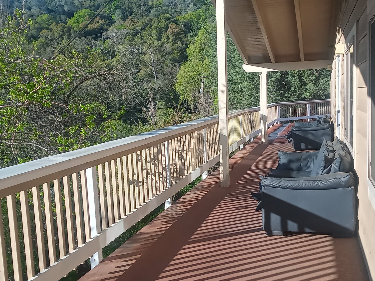 A sunny outdoor deck with wooden railings and patio furniture, overlooking lush green trees.