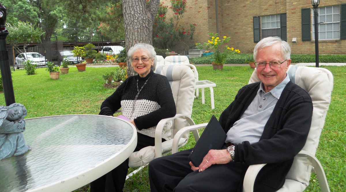 An elderly couple sitting outside in a garden, enjoying the day and smiling.