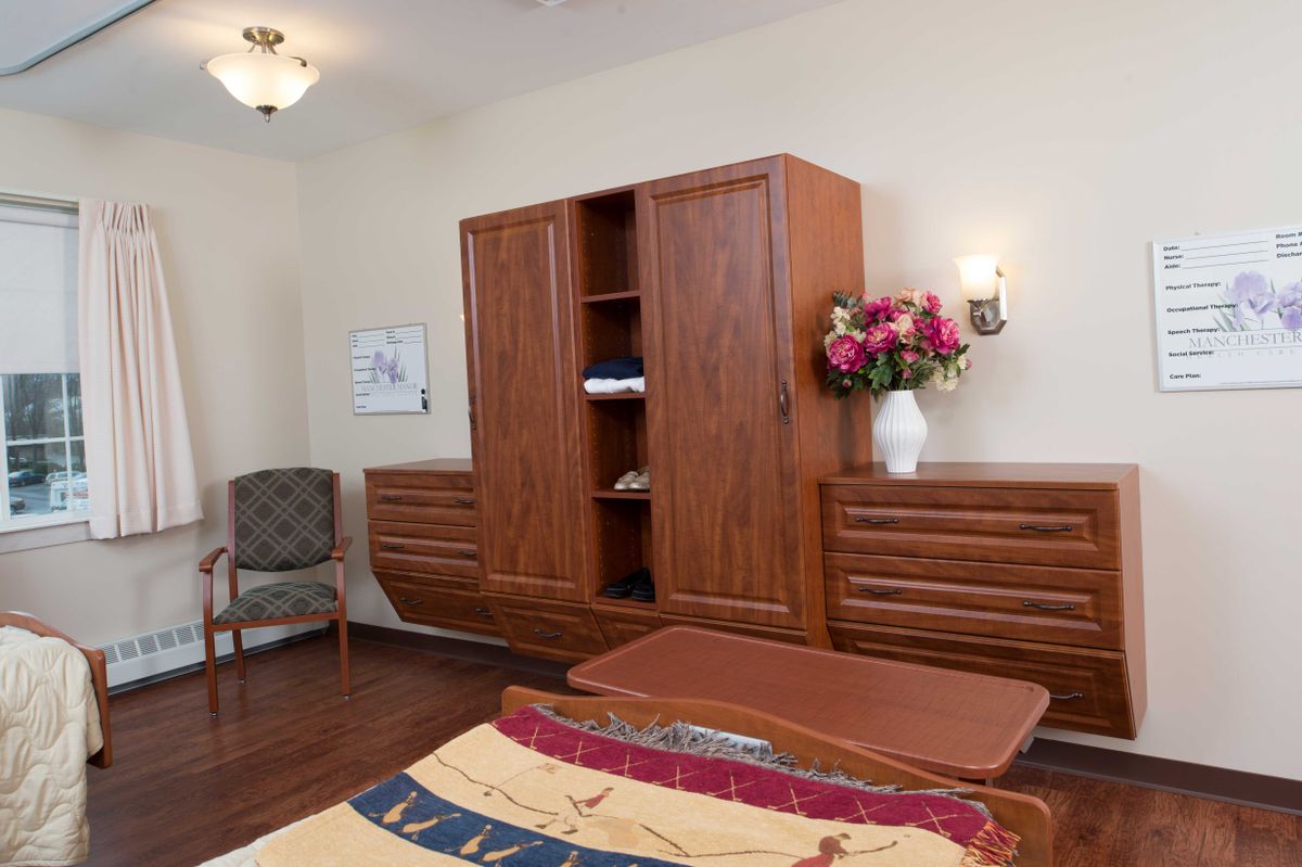 A cozy room with a wooden wardrobe, dresser, and a vase of flowers on display.