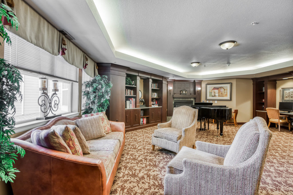 A cozy living room with a sofa, armchairs, bookshelf, and a piano.