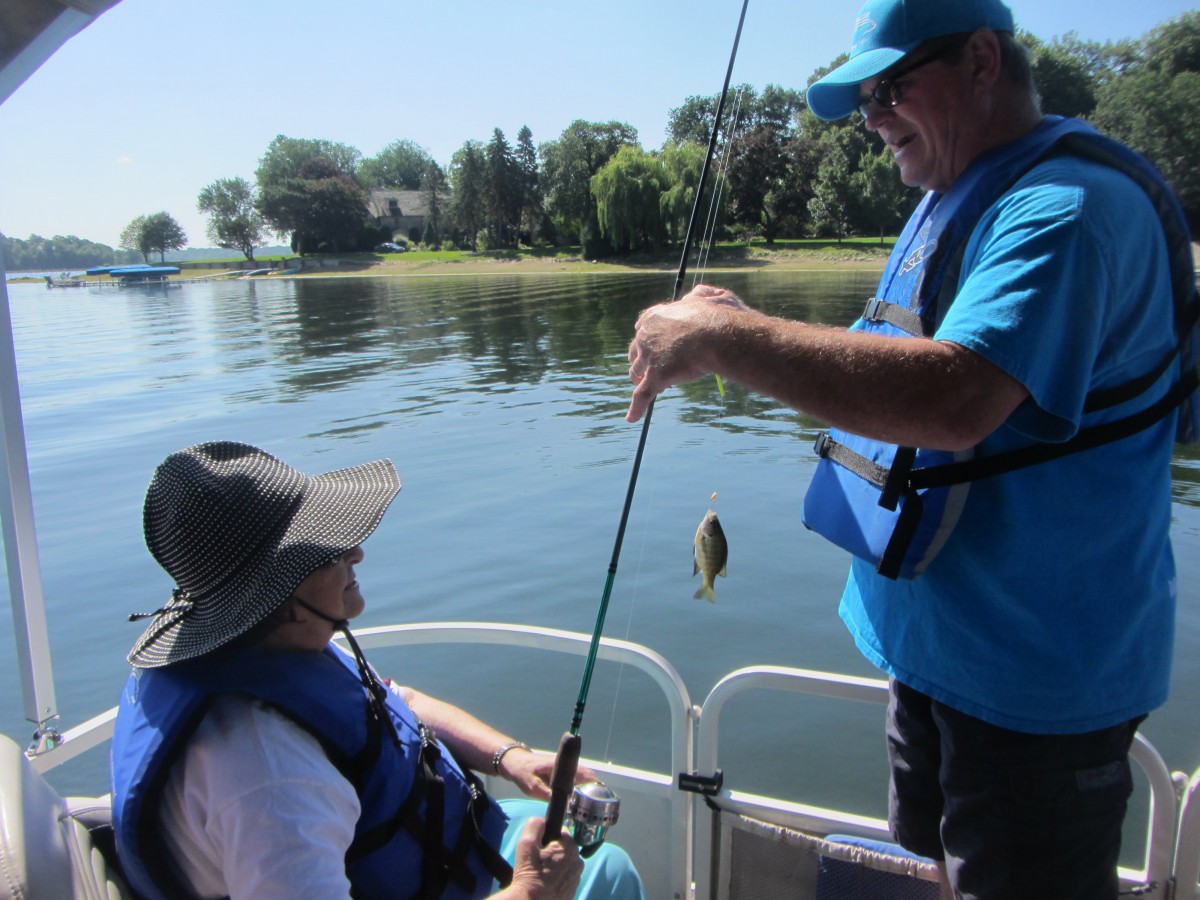 Two people fishing on a boat in a lake.