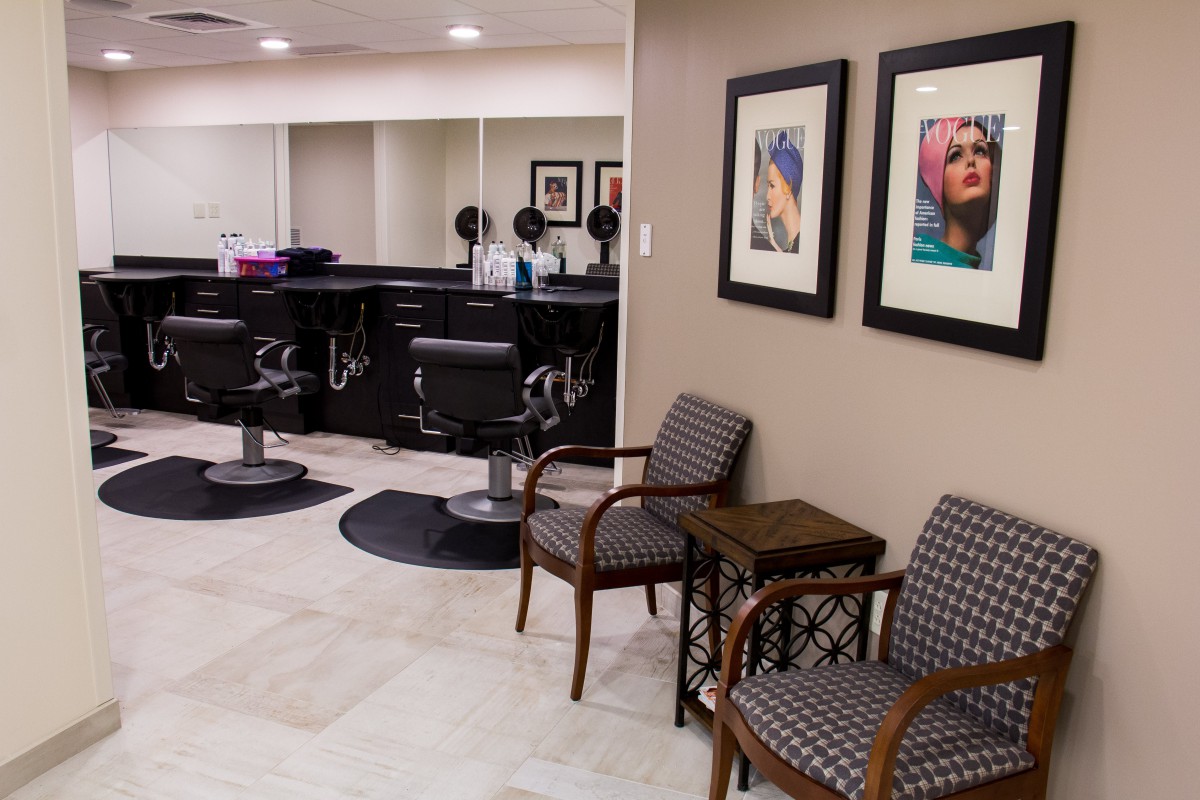 A modern hair salon interior featuring styling stations, comfortable waiting chairs, and framed artwork on the walls.