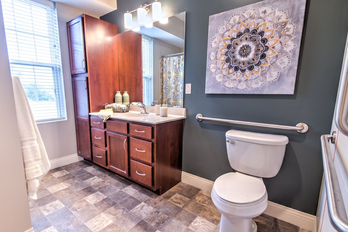 A modern bathroom with a wooden cabinet, sink, toilet, and decorative artwork on the wall.