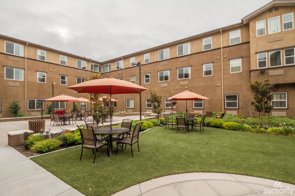 A courtyard with tables and umbrellas, surrounded by a brick building.