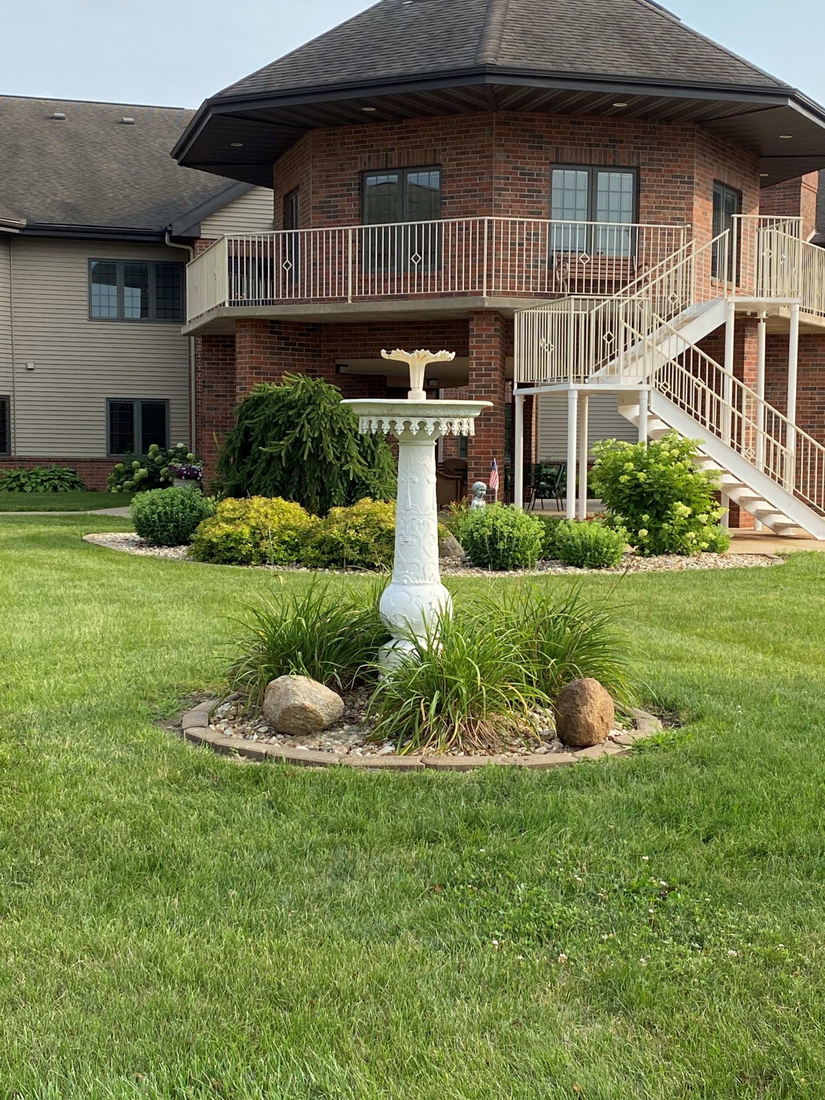 A well-maintained garden with a birdbath centerpiece in a residential backyard.