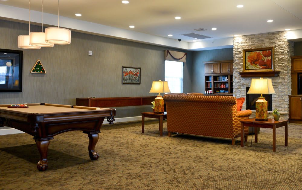 A cozy lounge area with a pool table, comfortable seating, and a bookshelf.