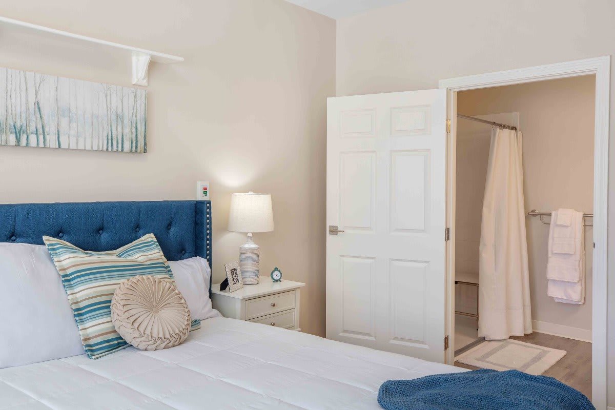 A cozy bedroom with a blue headboard, decorative pillows, and a bedside lamp.