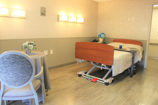 A well-lit hospital room featuring a patient bed, a small table with chairs, and warm decor.