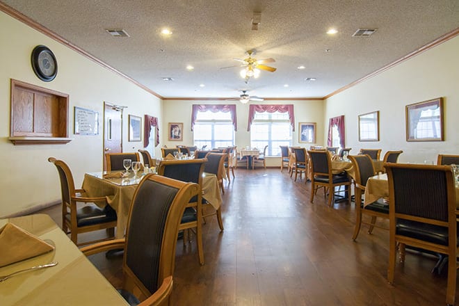 An empty dining room with neatly arranged tables and chairs, featuring large windows and elegant decor.