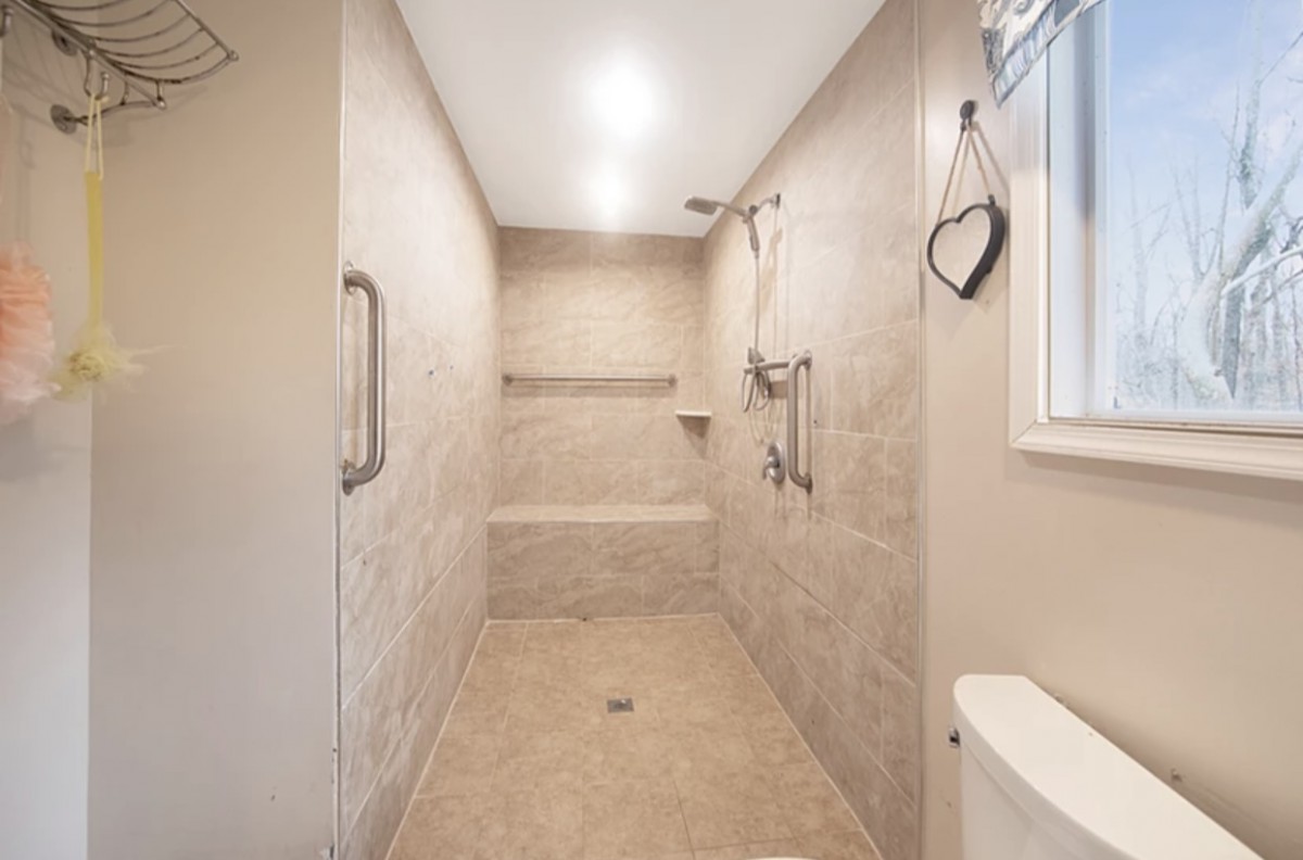 A modern walk-in shower with neutral tiles, featuring grab bars and a built-in bench.