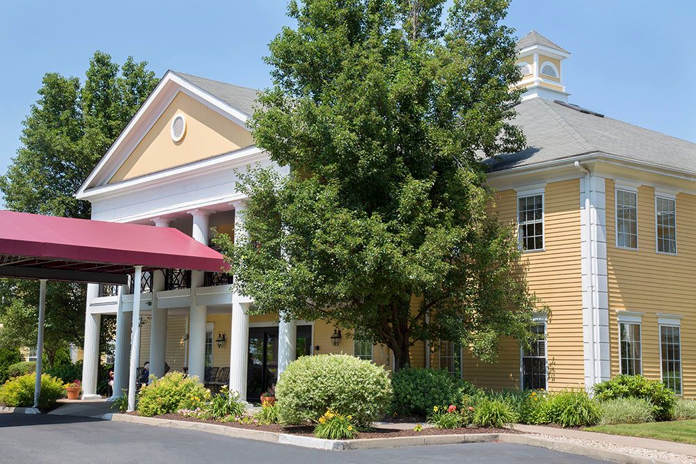 A picturesque building with a columned entrance surrounded by lush trees and landscaping.