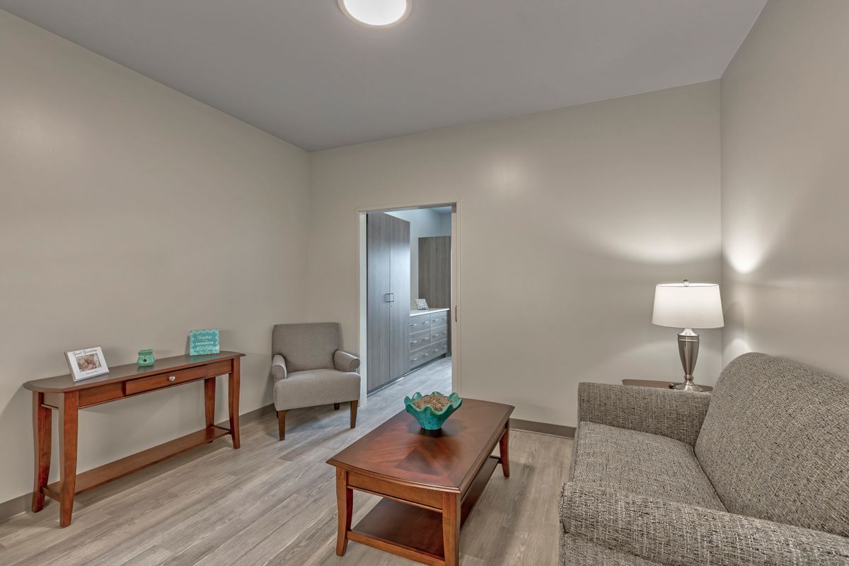 A modern living room with neutral tones, featuring a sofa, armchair, coffee table, and lamp.