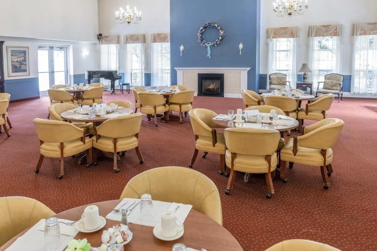 A spacious dining room with neatly set tables and a fireplace in a well-lit setting.