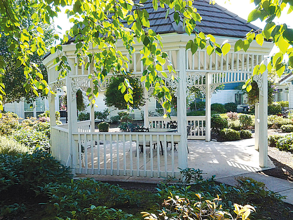 A charming white gazebo surrounded by lush greenery in a garden setting under dappled sunlight.