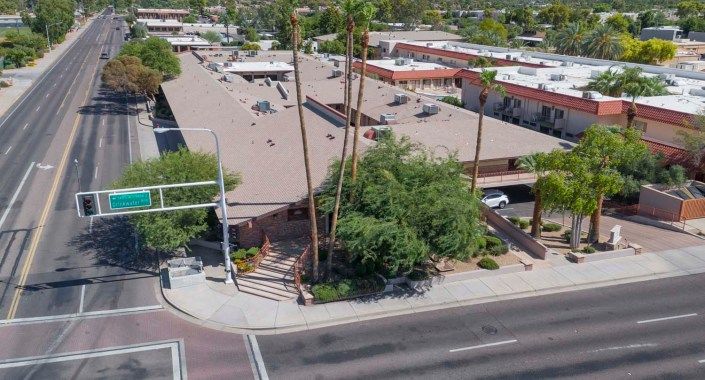 Aerial view of an urban building surrounded by palm trees at a road intersection.