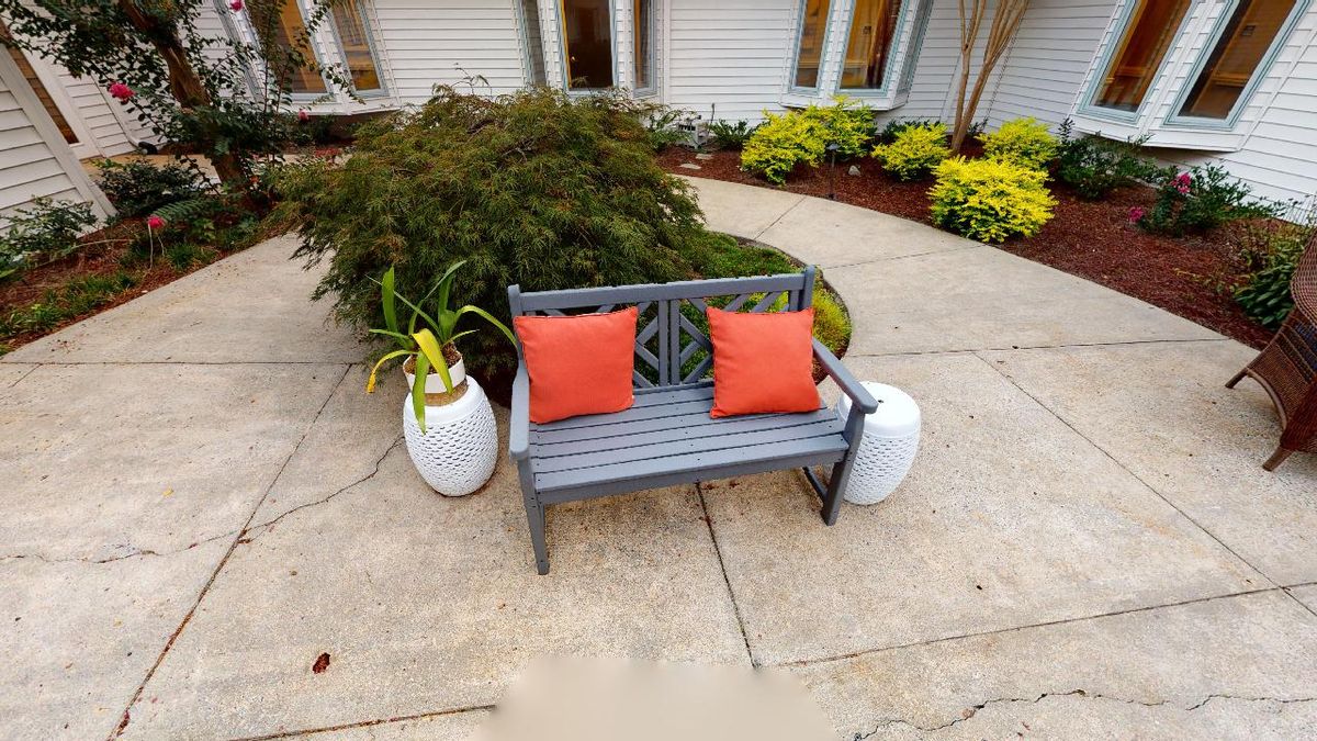 An inviting outdoor bench with orange cushions surrounded by greenery and potted plants.