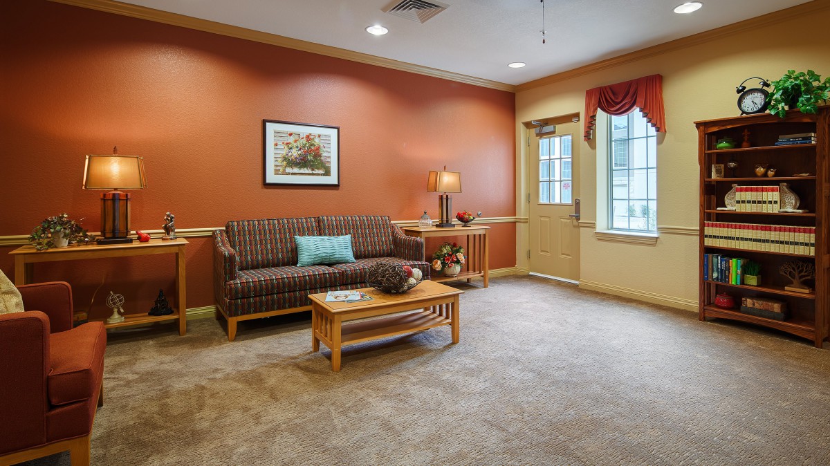 A cozy living room with orange walls, featuring a sofa, coffee table, and a lamp by the window.