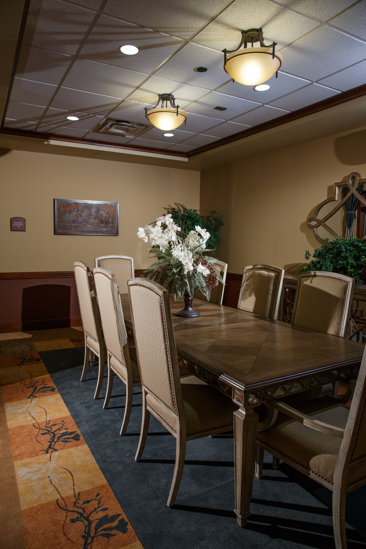 A cozy dining room with a large table, surrounded by chairs, decorated with flowers and plants.