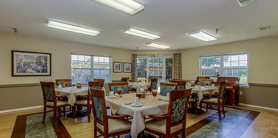 A well-lit dining room with set tables and chairs, featuring large windows and decorative elements.