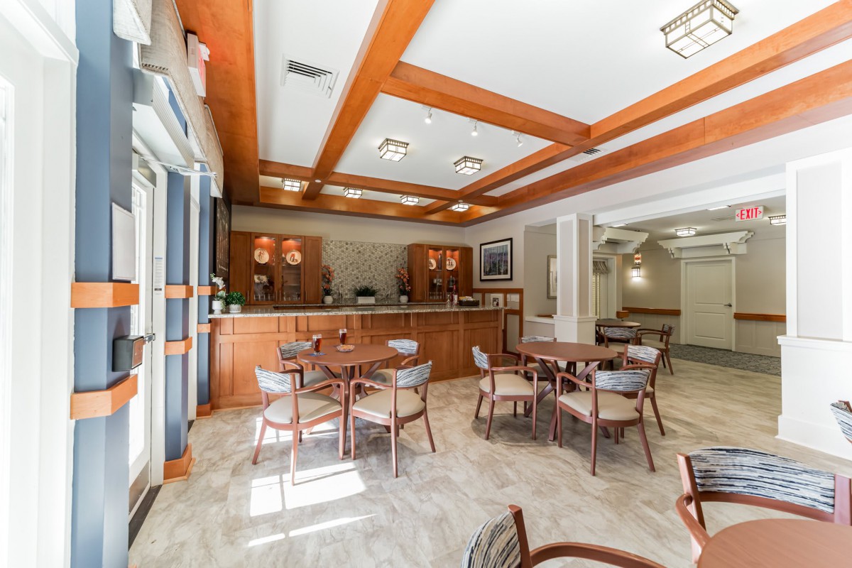 A cozy cafe interior with wooden beams and natural light, featuring tables, chairs, and a bar area.